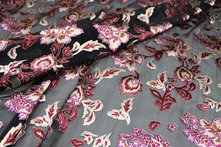 a close-up view of a fabric with a floral pattern in shades of red, pink, and white. The fabric appears to be a dark gray color, and the pattern is intricate and detailed, with the flowers and leaves covering the entire fabric surface.