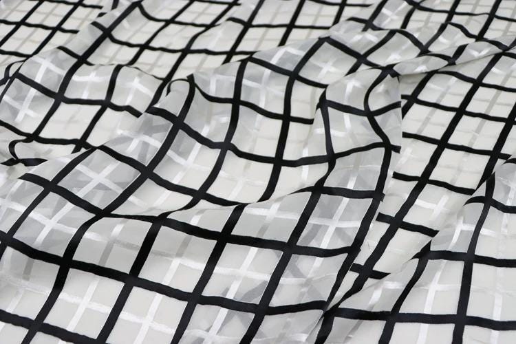 a close-up view of a fabric with a black and white checkered pattern. The fabric appears to be made of a sheer material, with a grid-like design that creates a visually striking contrast between the black and white elements.