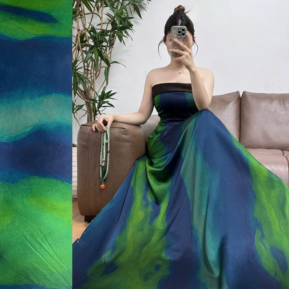 A woman in a long, colorful dress is sitting on a couch, taking a selfie with her phone.