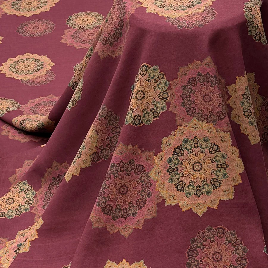 a close-up view of a fabric with a repeating pattern of colorful floral designs in shades of red, pink, and green. The fabric appears to be folded or draped, creating a visually appealing and intricate design.