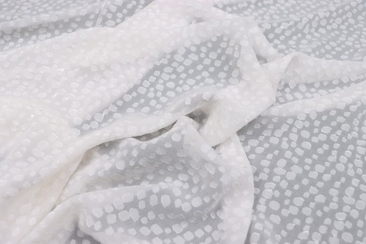 a close-up view of a white fabric with a polka dot pattern. The fabric appears to be crumpled and wrinkled, giving it a casual and relaxed appearance.