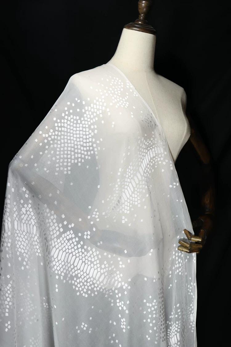 A mannequin wearing a white fabric with a pattern of small white dots or squares.