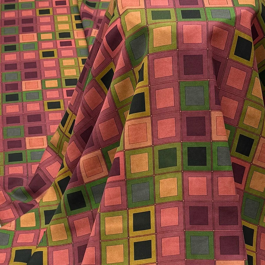 a close-up view of a fabric with a vibrant geometric pattern of squares in various colors, including shades of red, green, yellow, and black. The fabric appears to be folded or crumpled, creating a visually interesting texture.