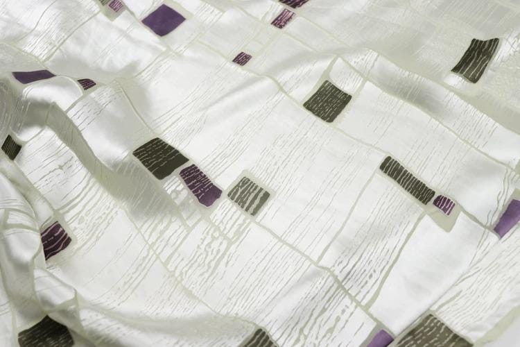 a close-up view of a white fabric with a pattern of purple and gray squares and rectangles.