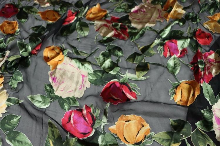 a close-up view of a fabric with a floral pattern of red, yellow, and pink roses. The fabric appears to be black, with the roses and leaves creating a vibrant and colorful design.