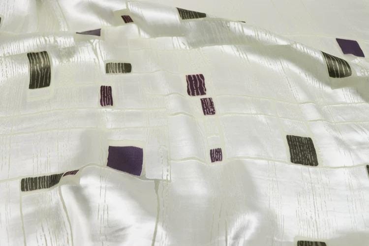a close-up view of a white fabric with a pattern of purple and black squares and rectangles.