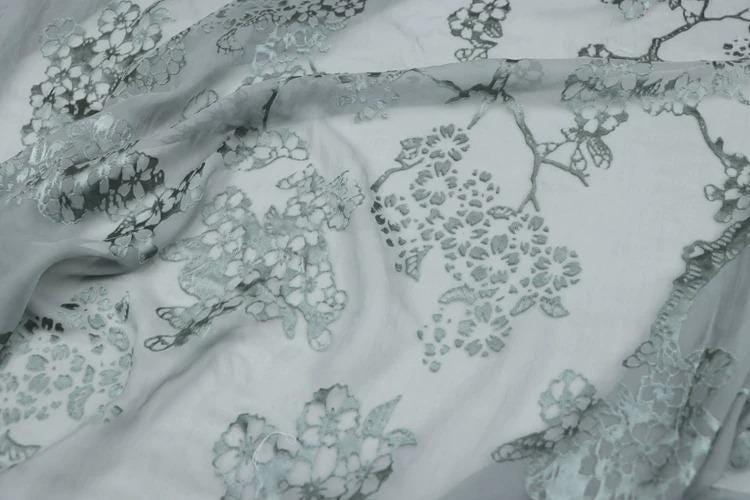 a close-up view of a fabric with a floral pattern, featuring various shades of gray and white.