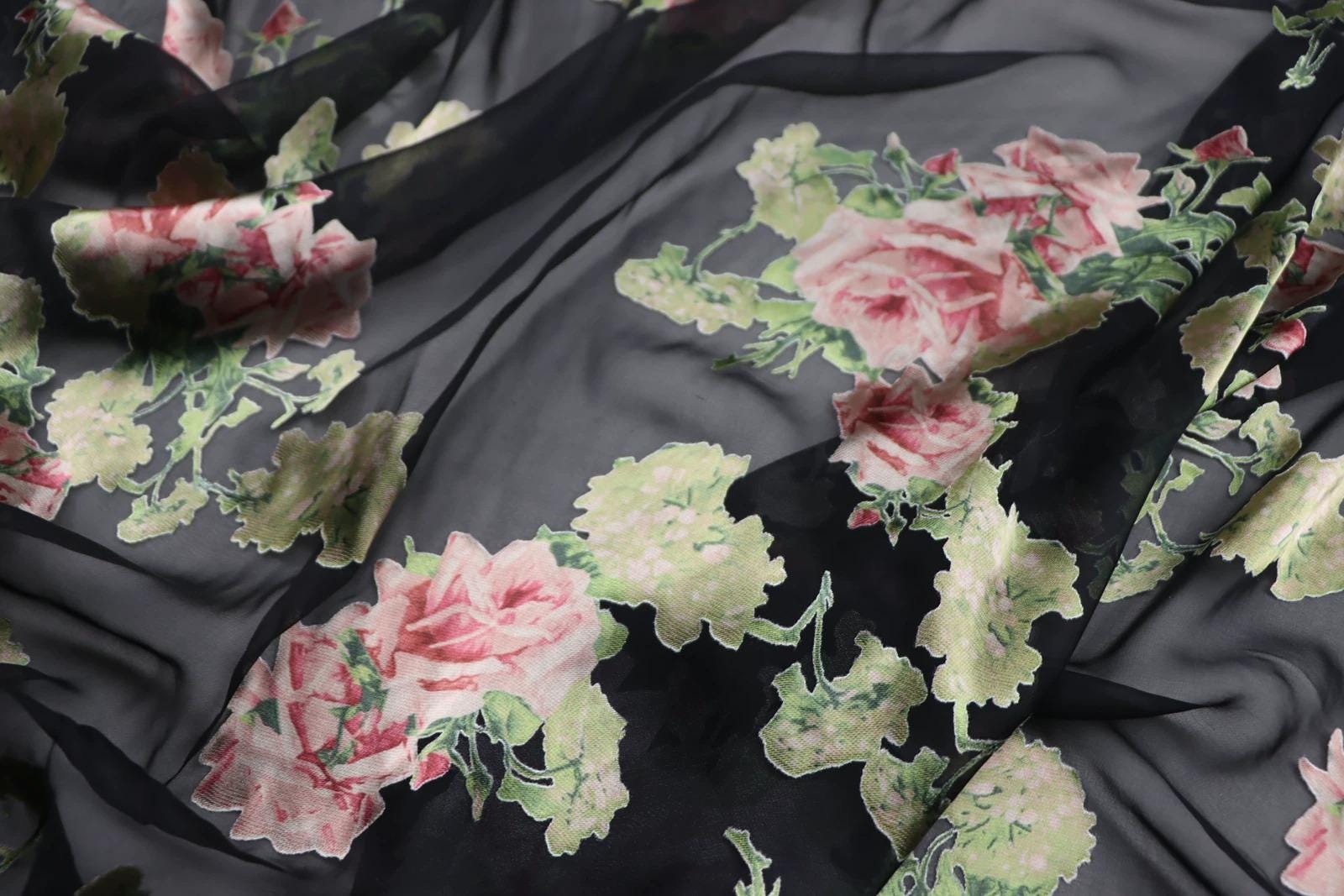 a close-up view of a fabric with a floral pattern, featuring pink and green flowers against a black background.