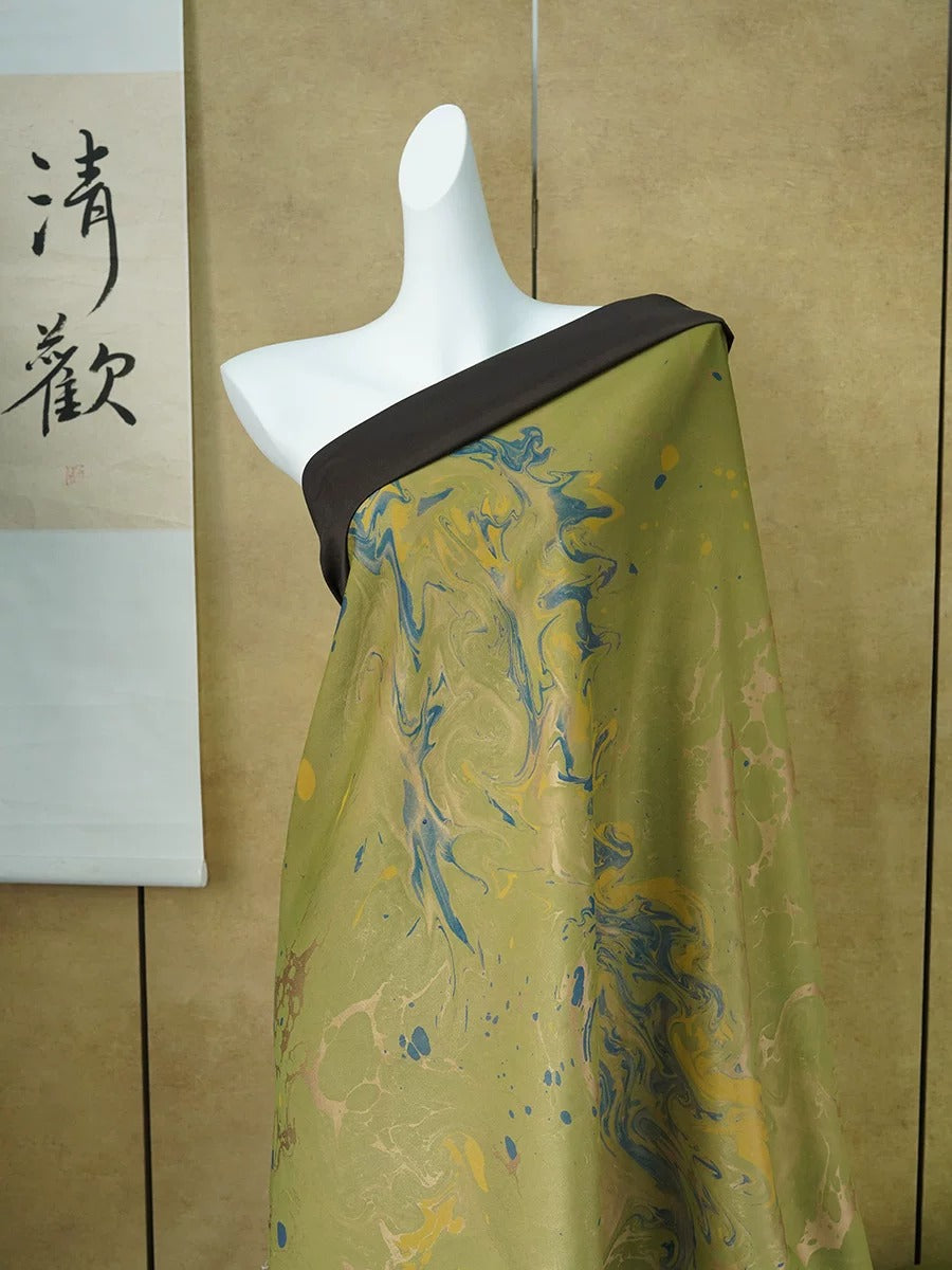 A mannequin wearing a green and blue patterned fabric draped over its shoulder, displayed against a beige wall with a Chinese character sign.