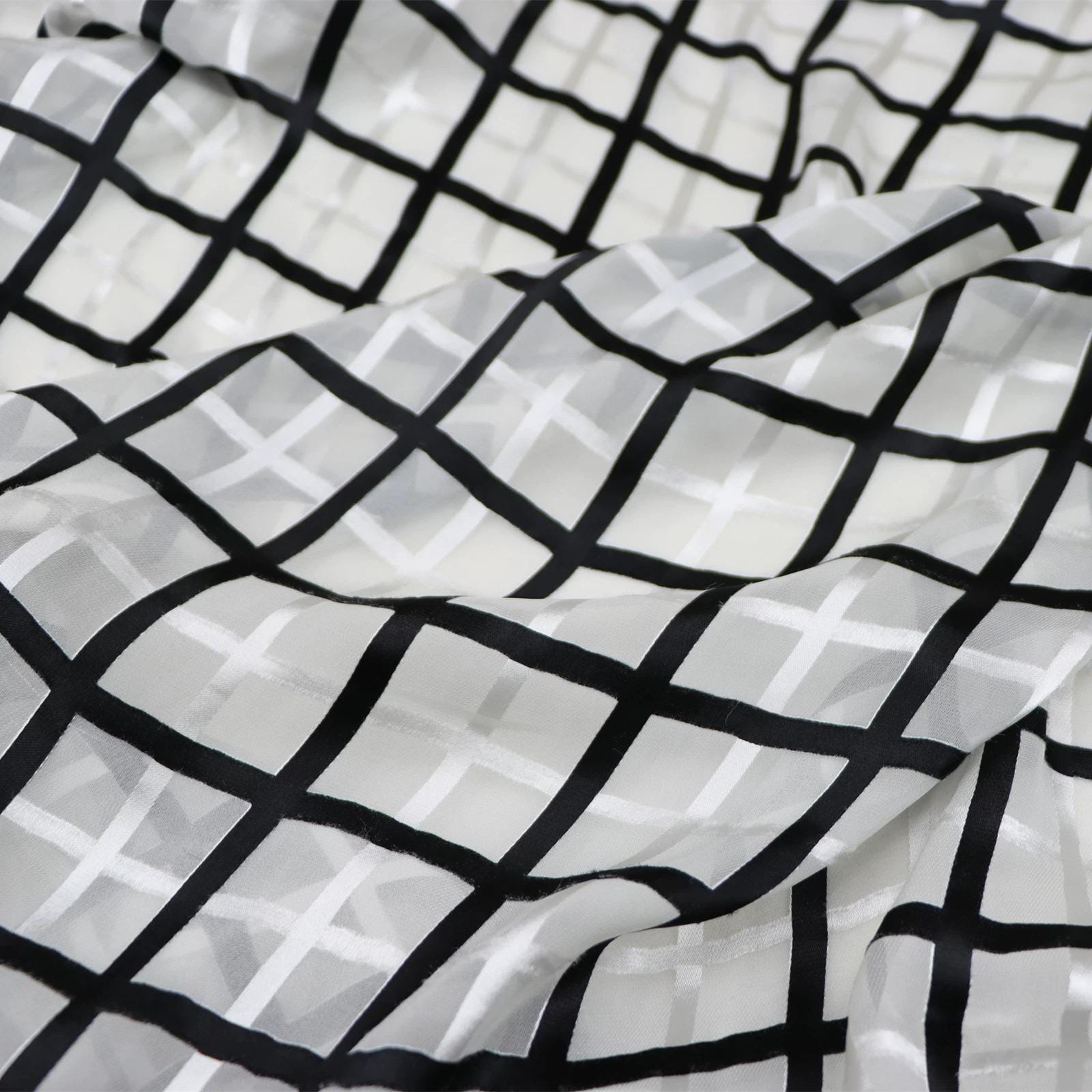 a close-up view of a fabric with a black and white checkered pattern. The fabric appears to be made of a sheer material, with a grid-like design of black and white lines covering the entire surface.