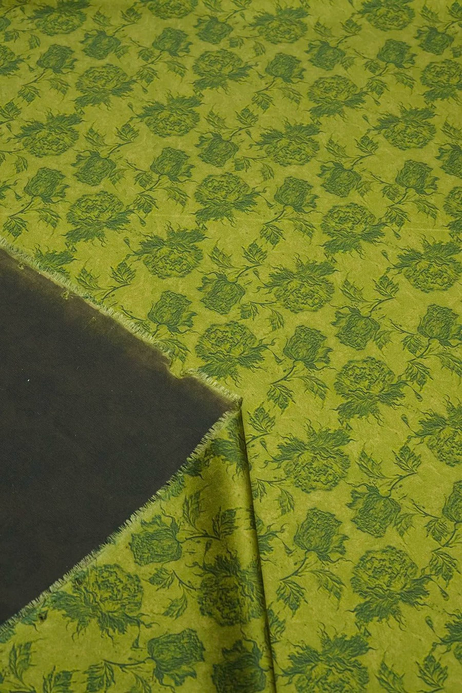 a close-up view of a fabric with a repeating pattern of green flowers on a dark background.