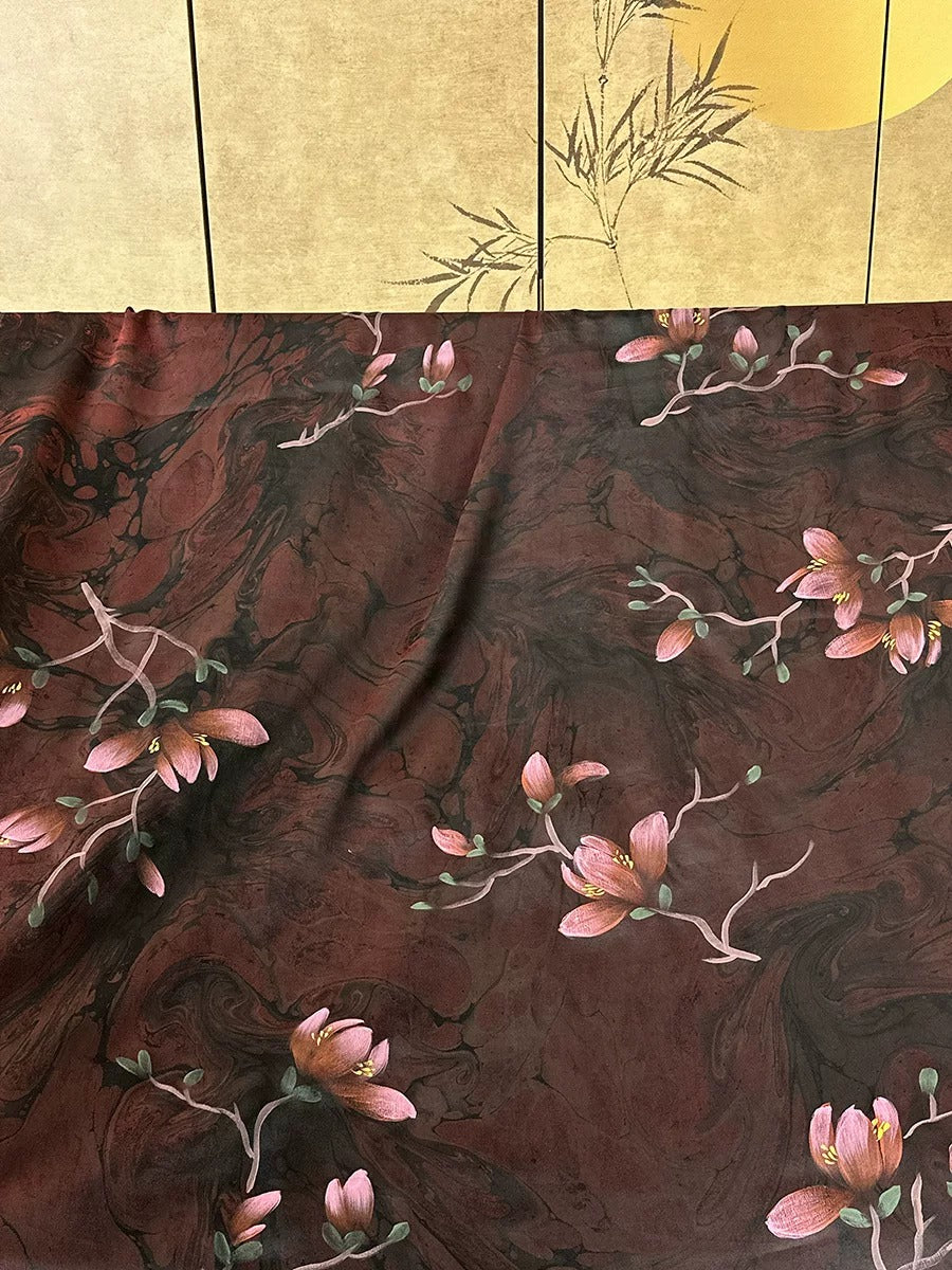 a close-up view of a dark red fabric with a floral pattern, including pink flowers and green leaves. The fabric appears to be made of a soft, plush material, and the floral design is intricate and detailed.