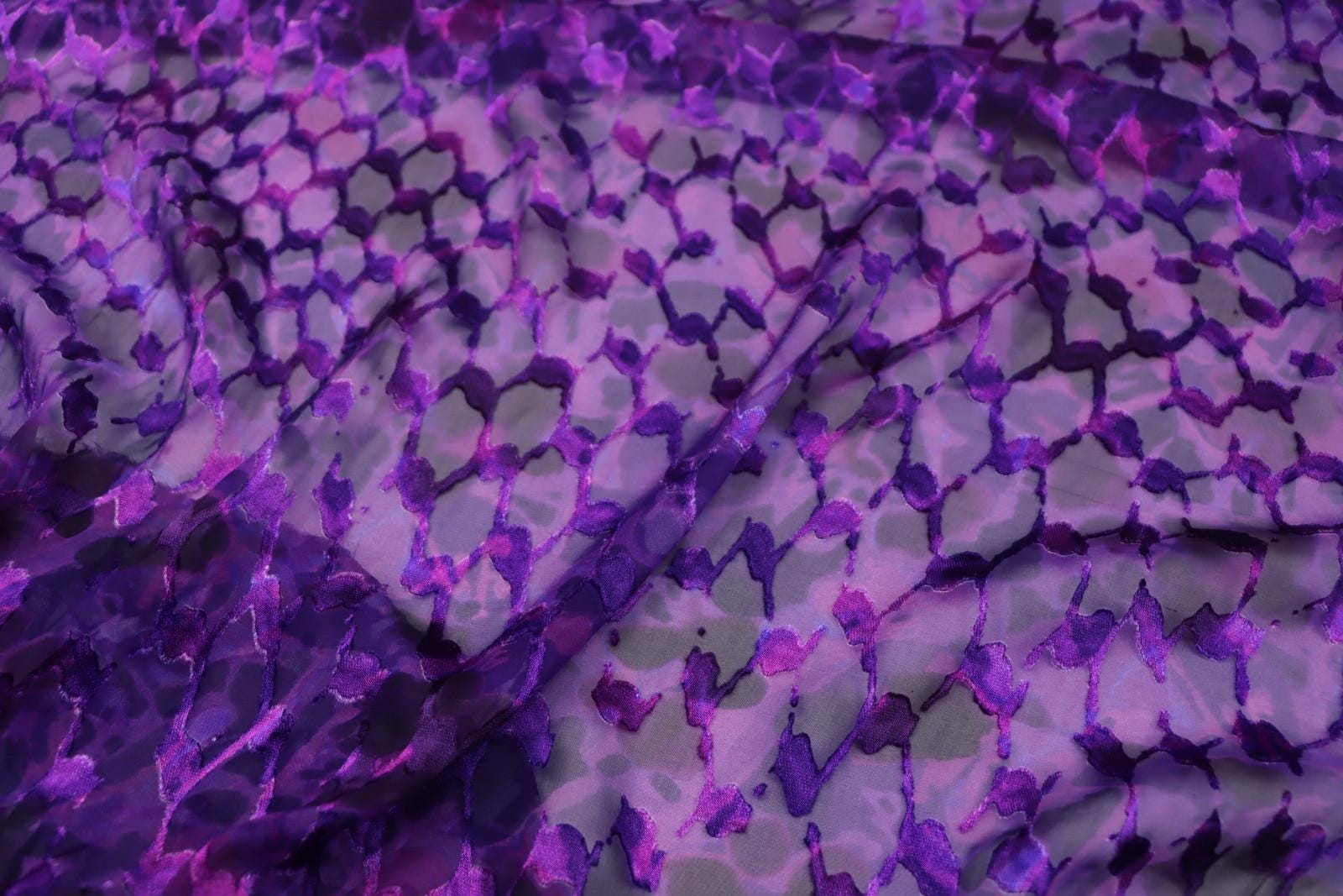 a close-up view of a fabric with a purple and gray pattern, featuring a repeating geometric design.