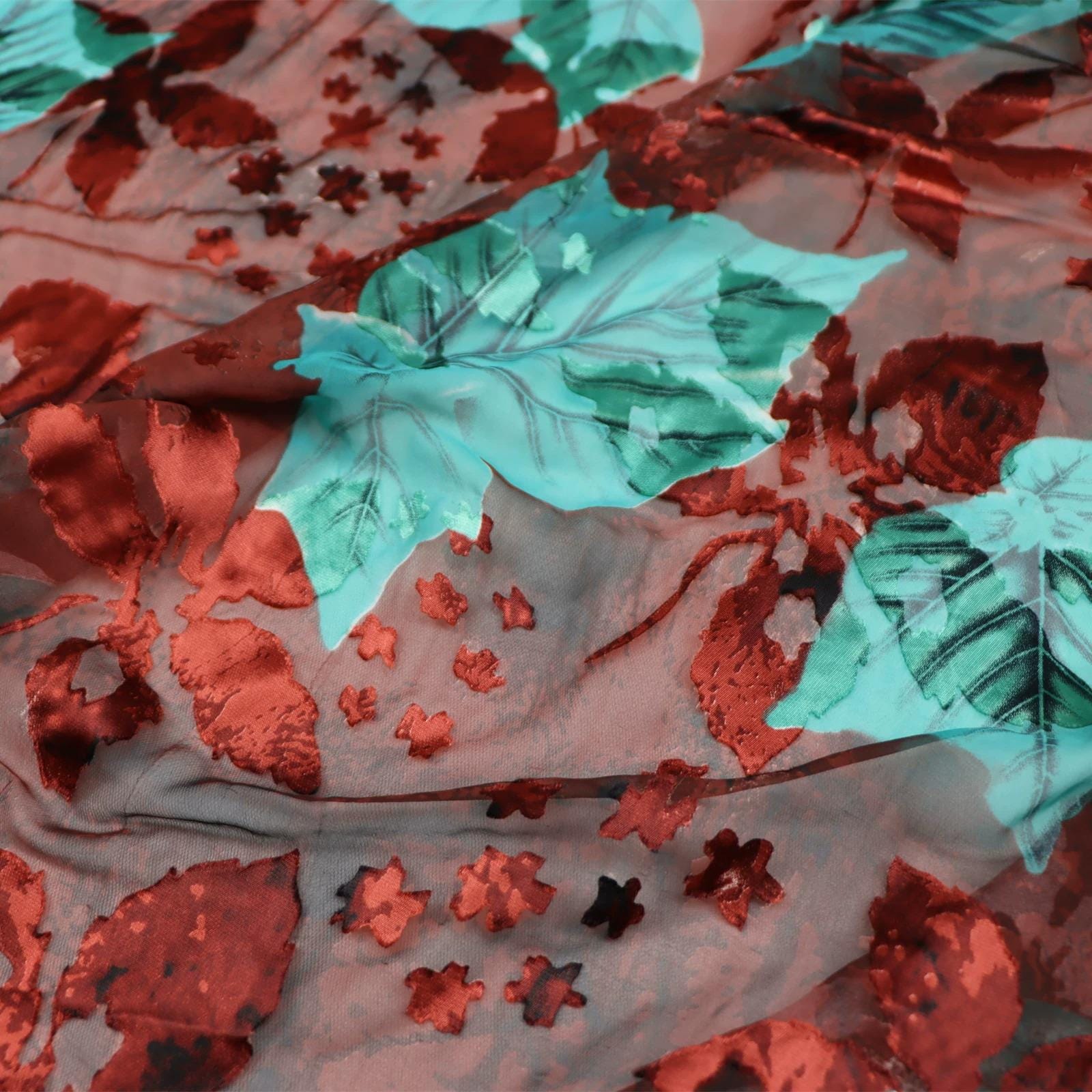 The image is a close-up view of a fabric with a floral pattern, featuring red and green leaves and small red flowers. The fabric appears to be made of a sheer material, giving it a delicate and airy appearance.