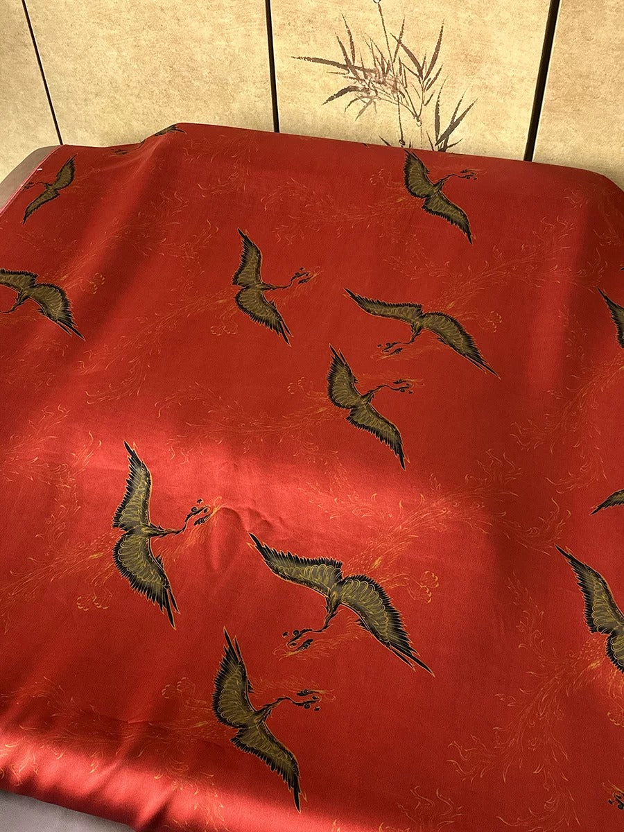a red fabric with a repeating pattern of black and gold birds in flight.