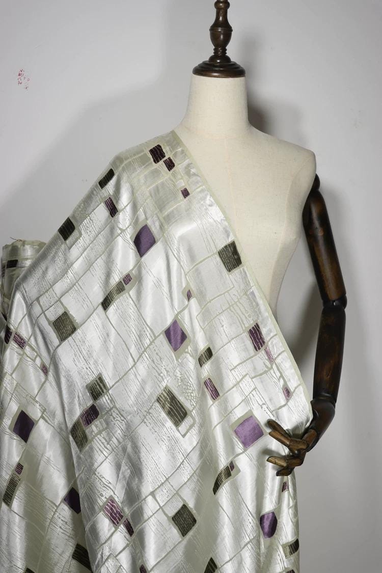 A mannequin wearing a white dress with a patterned fabric draped over it.