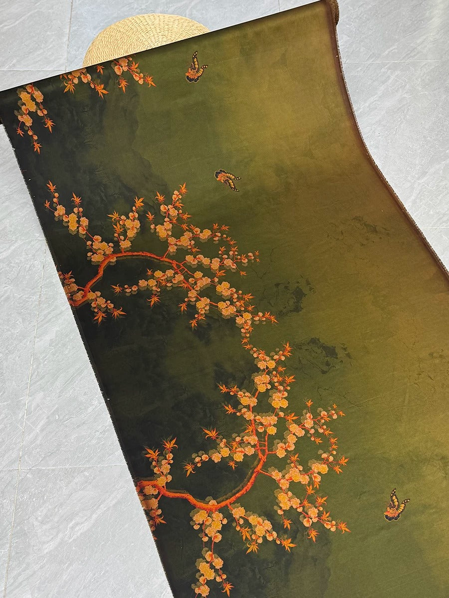 a close-up view of a decorative fabric with a floral pattern. The fabric has a dark green background with orange and yellow flowers and butterflies. The fabric appears to be rolled up and placed on a surface.