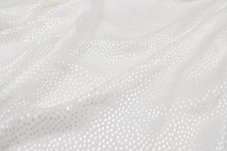 The image is a close-up of a white fabric with small white dots or polka dots, creating a textured and shiny appearance.