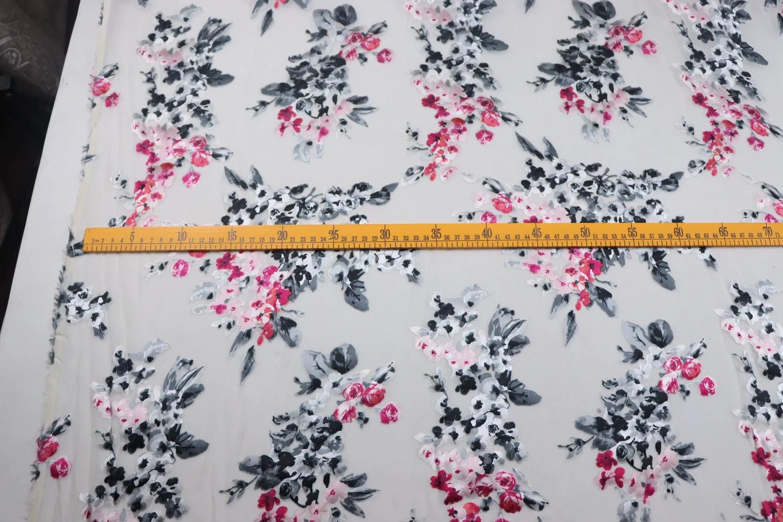 a fabric with a floral pattern, featuring a yellow ruler placed on top of it.