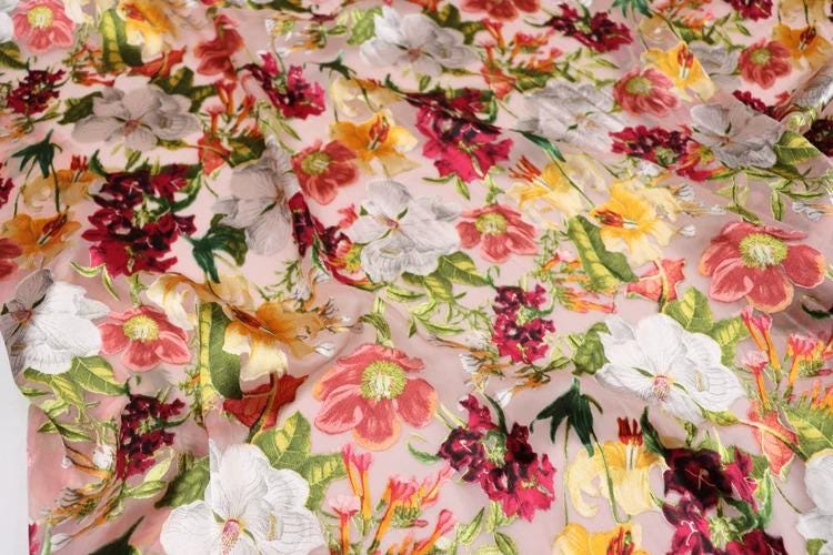 a close-up view of a fabric with a vibrant floral pattern. The fabric is covered in a variety of colorful flowers, including red, yellow, and white flowers, as well as green leaves. The flowers are arranged in a visually appealing manner, creating a lively and eye-catching design.
