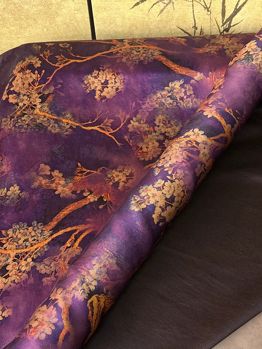 a close-up view of a fabric with a vibrant purple and gold floral pattern. The fabric appears to be a piece of material, possibly a piece of clothing or a textile, with a rich, colorful design. The fabric is displayed against a contrasting background, which further accentuates its visual appeal.