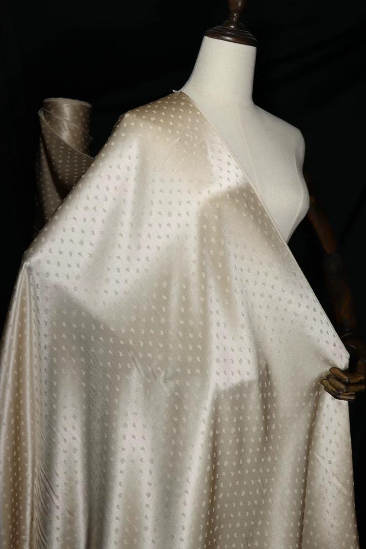 A mannequin wearing a beige fabric with small white polka dots, displayed against a dark background.