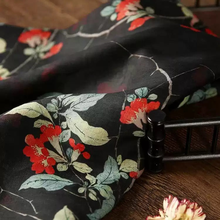 a close-up view of a black fabric with a floral pattern, featuring red and green flowers and leaves. The fabric appears to be a piece of clothing or textile, with a black metal frame visible in the background.