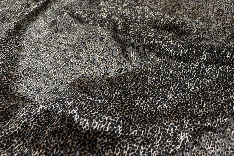 a close-up view of a fabric with a distinctive leopard print pattern. The fabric appears to be a blend of black and white colors, with the leopard print pattern adding a touch of wildness to the overall design.