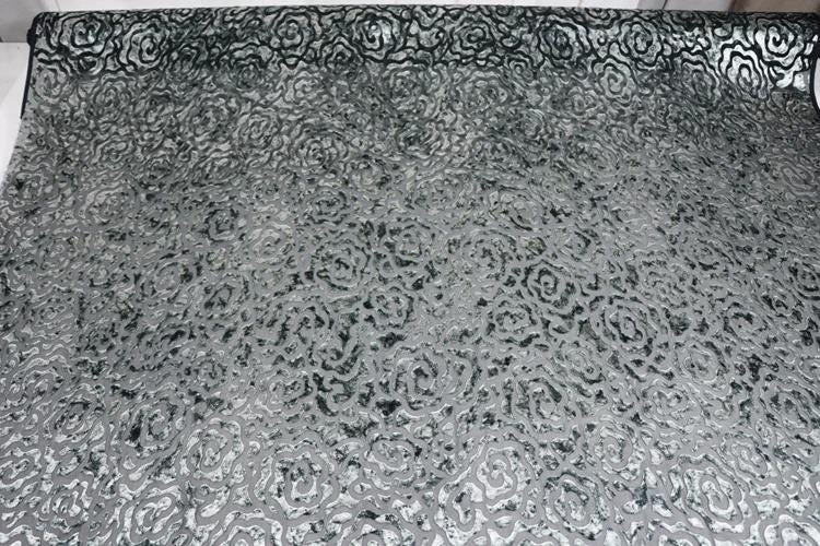 a close-up view of a fabric with a repeating pattern of black and white swirls or circles. The pattern is intricate and detailed, covering the entire surface of the fabric.