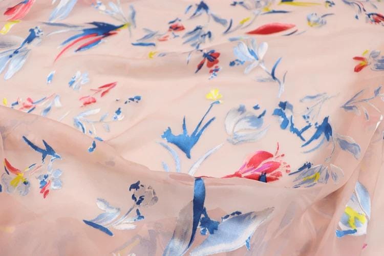 a close-up view of a fabric with a floral pattern, featuring various shades of pink, blue, and white flowers and leaves.