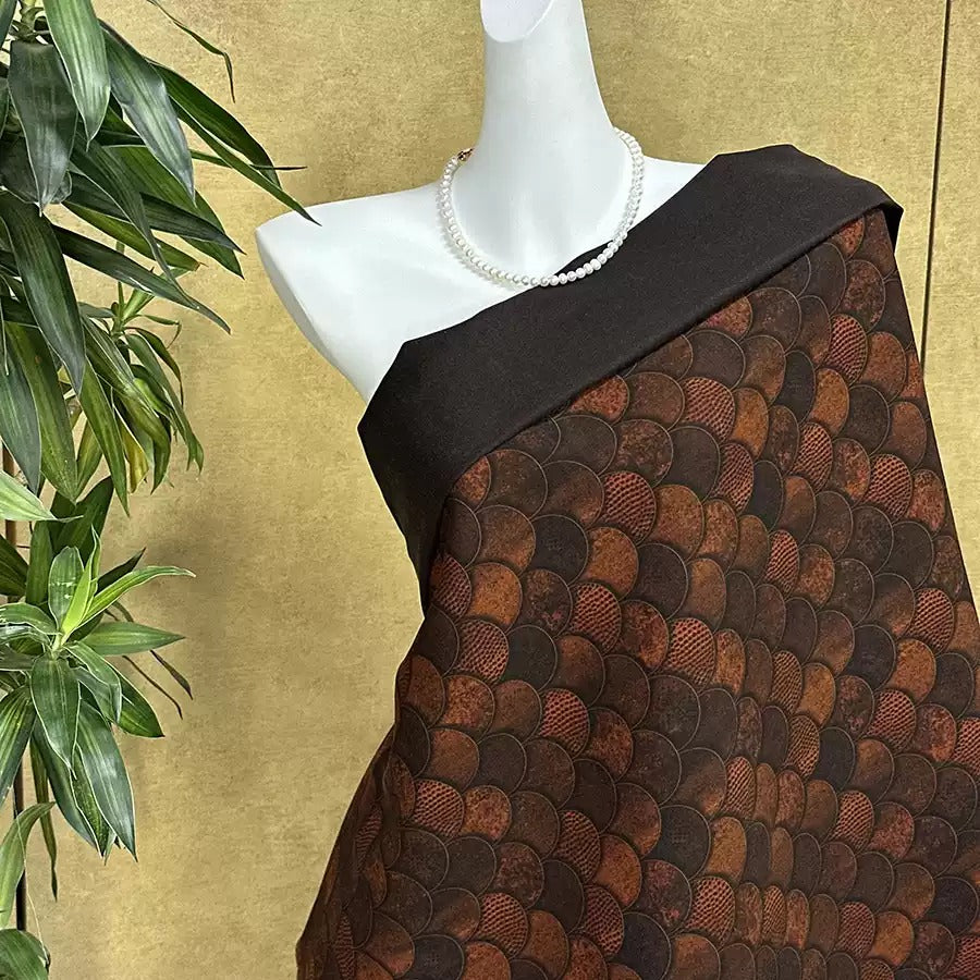 A mannequin wearing a black and brown patterned fabric draped over its body, with a pearl necklace visible.