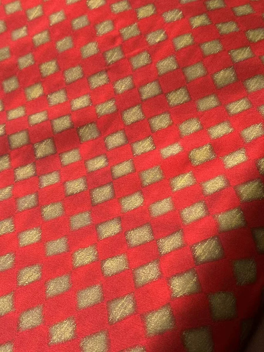 a close-up view of a red fabric with a gold pattern, featuring a repeating diamond-shaped design.