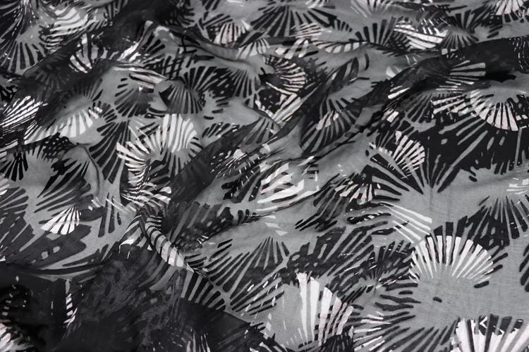 The image is a close-up view of a fabric with a black and white pattern, resembling a repeating design of leaves or flowers.