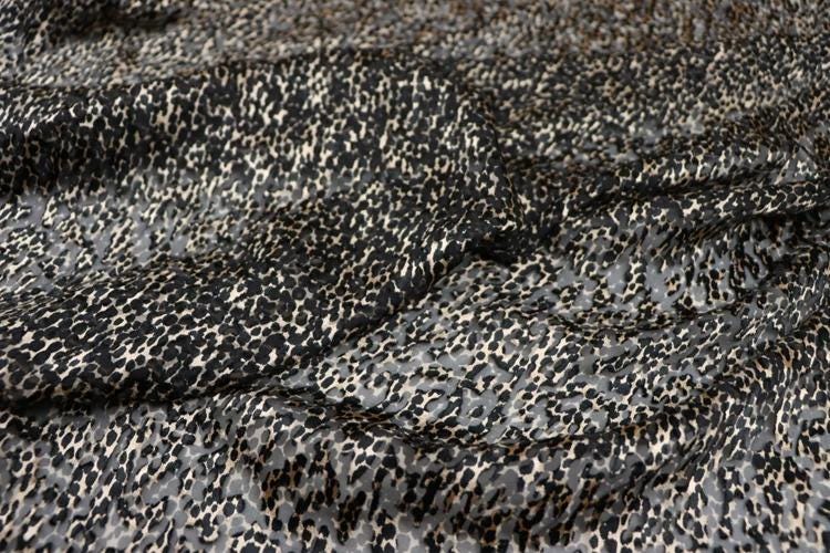 a close-up view of a fabric with a distinctive leopard print pattern. The fabric appears to be a blend of black and gray colors, creating a visually striking and textured appearance.