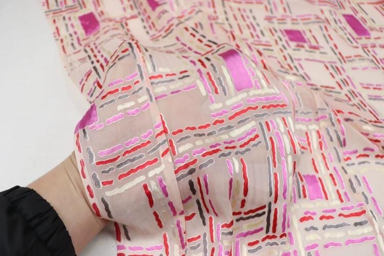 A close-up view of a hand holding a fabric with a geometric pattern in shades of pink, red, and gray.
