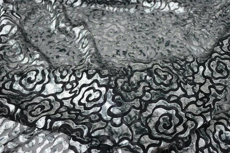 a close-up view of a fabric with a repeating pattern of black and white swirls or curves. The pattern appears to be a floral or abstract design, with the black and white colors creating a visually striking contrast.