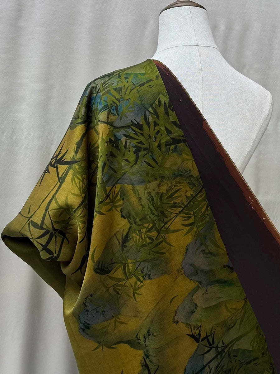 a mannequin wearing a colorful, patterned fabric with a mix of green and brown colors. The fabric appears to be a silk or satin material, and the design is inspired by nature, with a floral or leaf-like pattern. The mannequin is positioned against a plain background, allowing the vibrant colors and patterns of the fabric to stand out.
