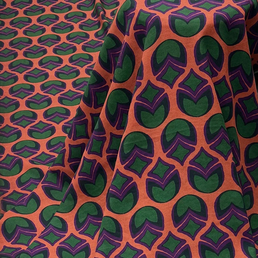 a fabric with a repeating pattern of green and orange circles on a dark background.