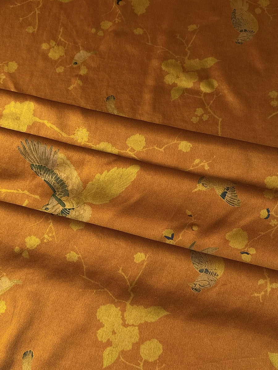 a close-up view of a fabric with a floral pattern in shades of orange and yellow. The fabric appears to be folded or crumpled, giving it a textured and wrinkled appearance.