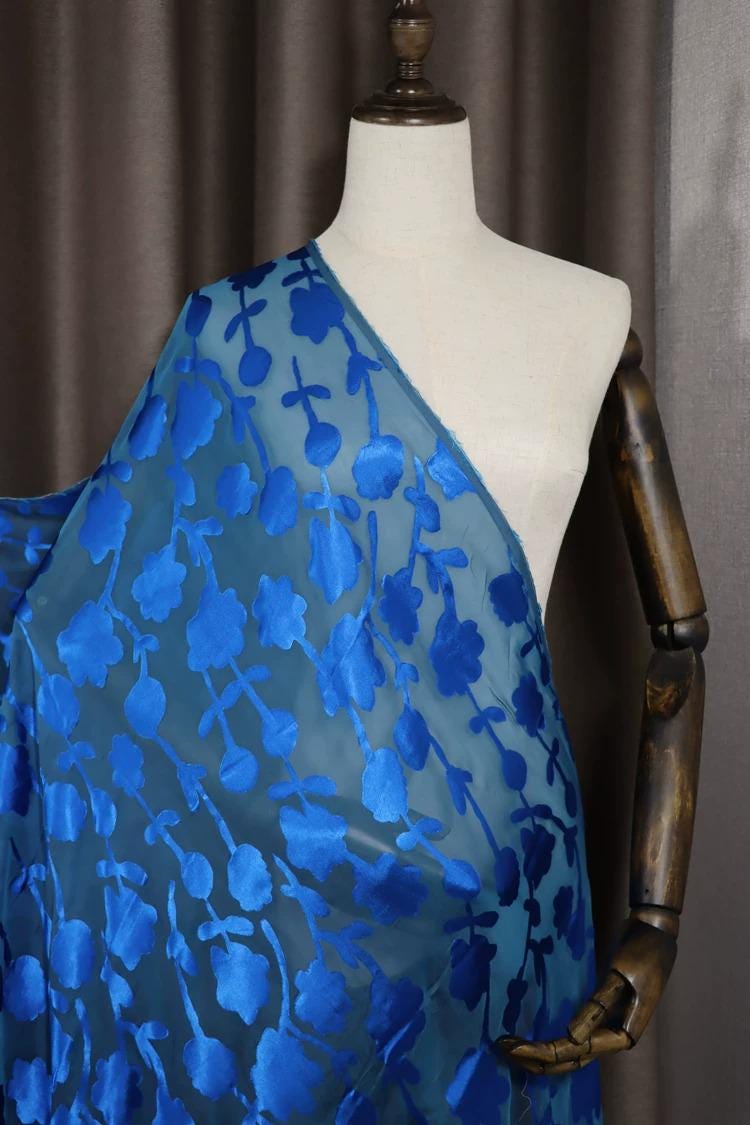 A mannequin wearing a blue fabric with a floral pattern, displayed on a wooden mannequin arm.