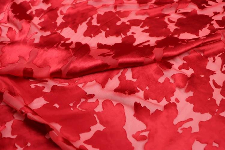 a close-up view of a fabric with a red floral pattern. The fabric appears to be made of a shiny, shiny material, possibly silk or satin, and has a slightly wrinkled texture. The pattern consists of red flowers or leaves, which are the main design element of the fabric. The fabric is spread out, covering a significant portion of the image, and the close-up view allows for a detailed examination of the intricate design.