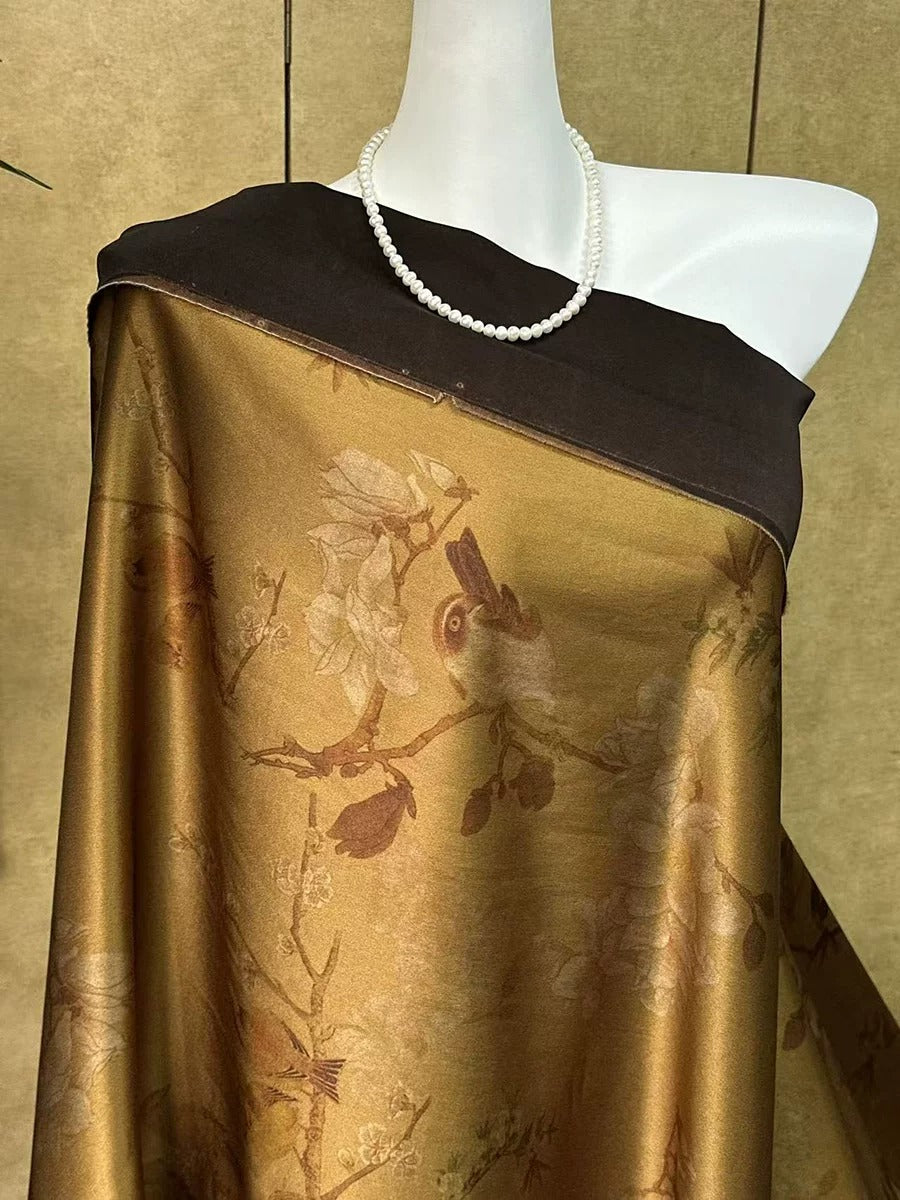 A mannequin wearing a gold and black patterned fabric with a white pearl necklace draped over it.