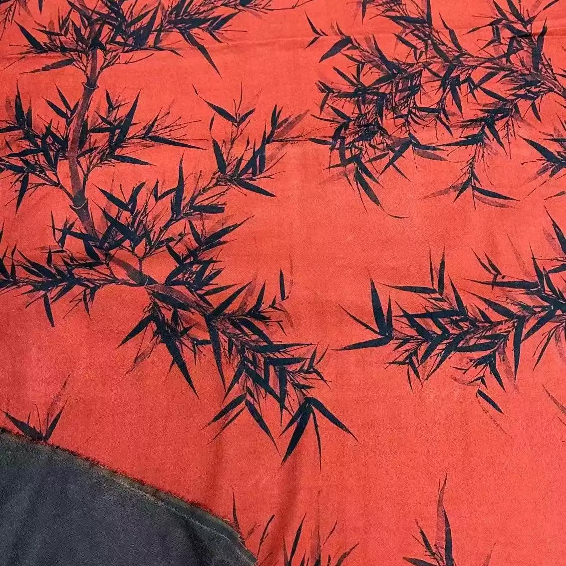a close-up view of a fabric with a striking red background adorned with black leaf patterns. The fabric appears to be a piece of clothing or textile, with the leaf patterns covering a significant portion of the surface.