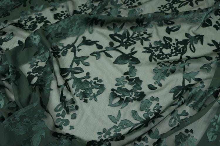 a close-up view of a fabric with a floral pattern, featuring a mix of dark and light green colors.