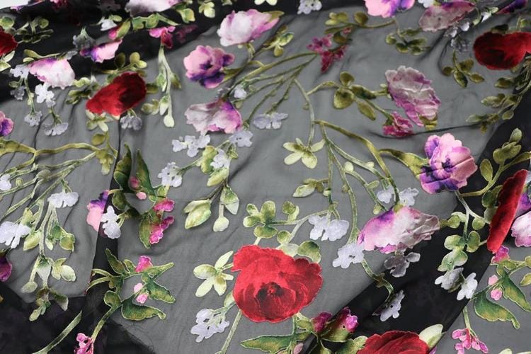 a close-up view of a fabric with a floral pattern. The fabric is predominantly gray, with red and purple flowers and leaves scattered across it. The flowers appear to be the main focus of the image, with the leaves providing a contrasting background. The overall composition of the image is visually appealing and showcases the intricate details of the floral pattern.