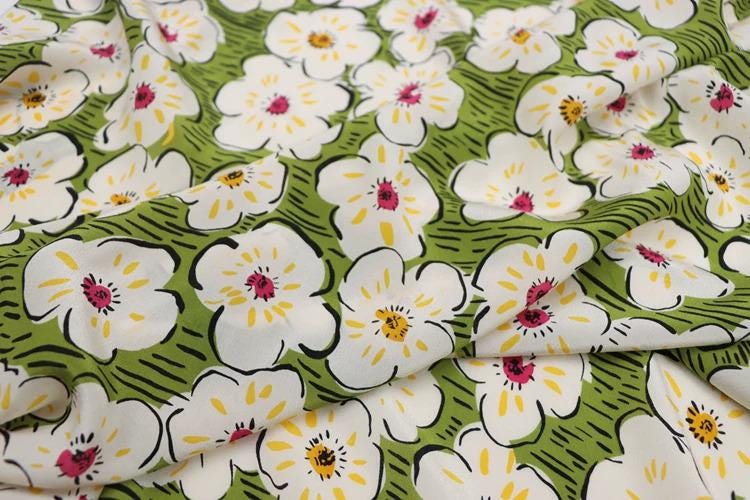 a close-up view of a fabric with a repeating pattern of white flowers with yellow centers against a green background.