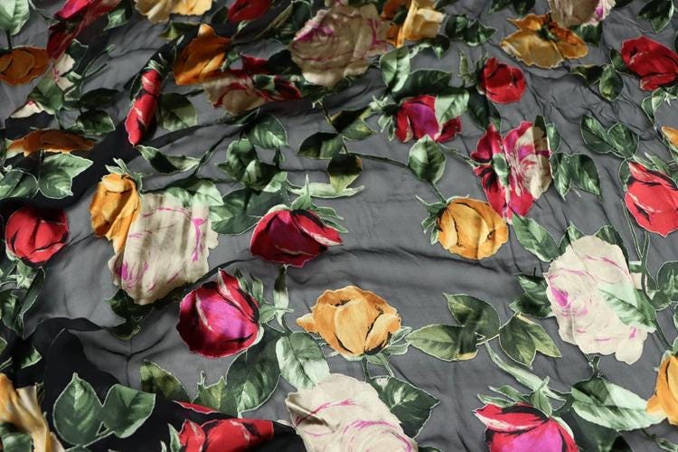 a close-up view of a fabric with a vibrant floral pattern. The fabric is predominantly gray, with red, yellow, and white flowers scattered across it. The flowers appear to be in various stages of unfolding, creating a dynamic and lively visual effect. The fabric is crumpled, adding a sense of texture and movement to the overall composition.