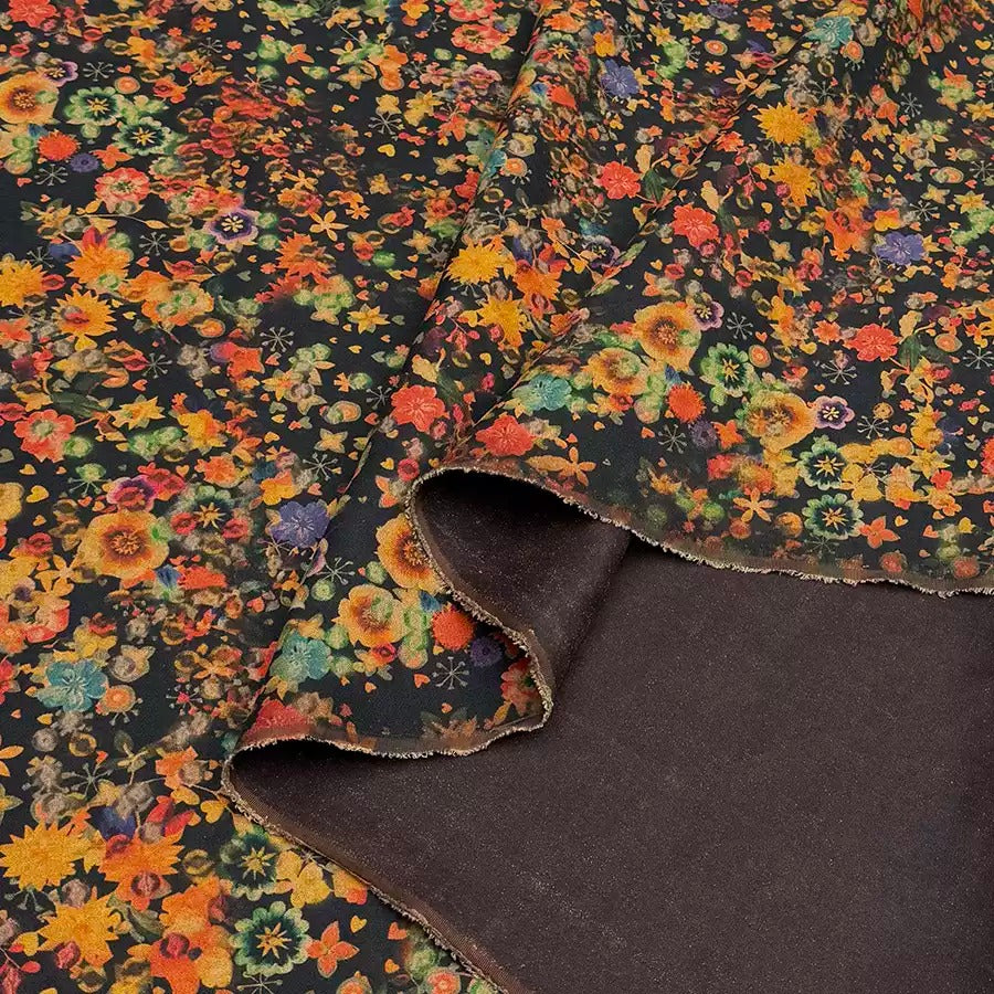 a close-up view of a fabric with a vibrant floral print in shades of orange, yellow, and green. The fabric appears to be a dark-colored material, possibly a dark-colored cotton or linen, with a noticeable texture. The image does not contain any text or other discernible objects or actions.