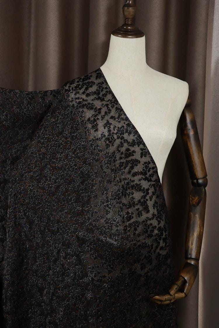 A mannequin wearing a black and gray patterned fabric draped over its body.