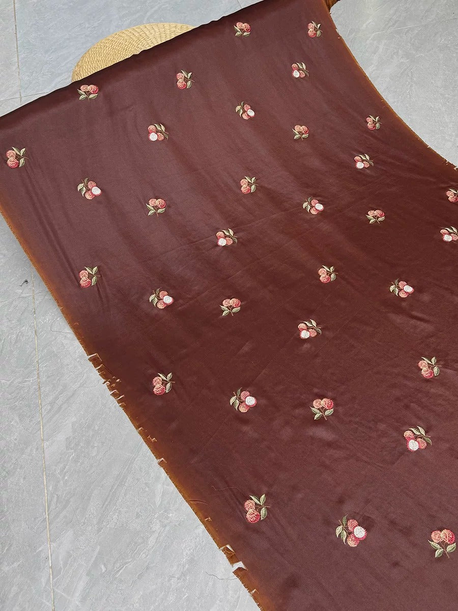 a close-up view of a brown fabric with a repeating pattern of small red cherries or berries embroidered on it.